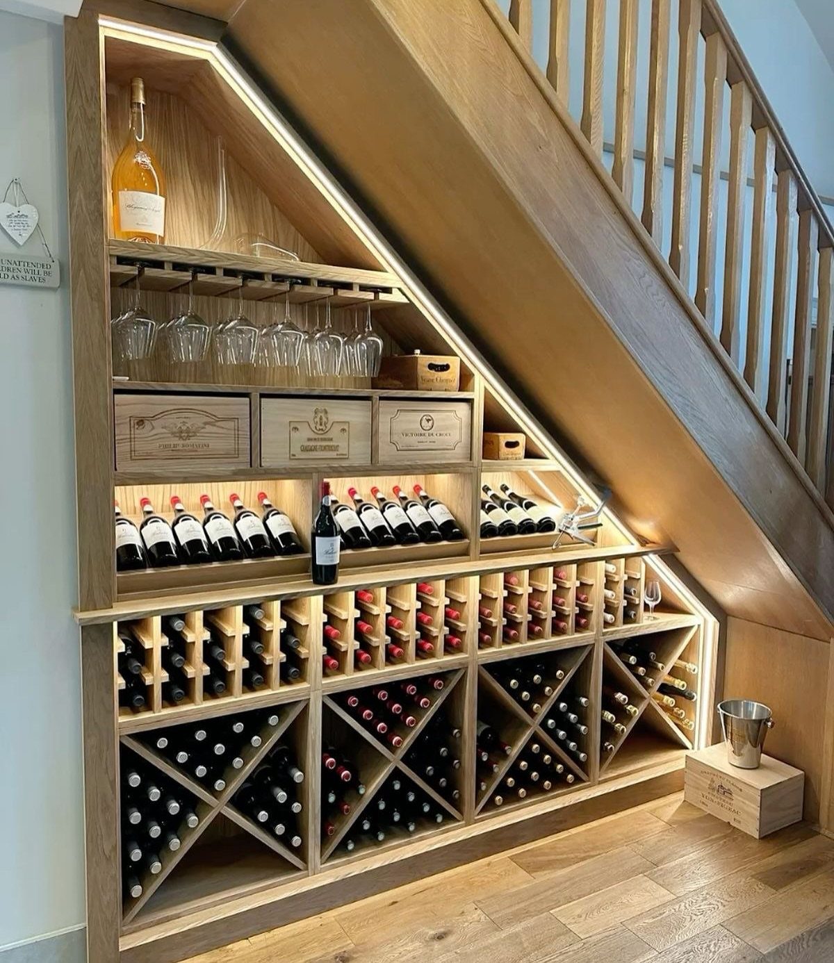 Custom wooden wine storage built into the triangular space underneath a staircase with integrated lighting.