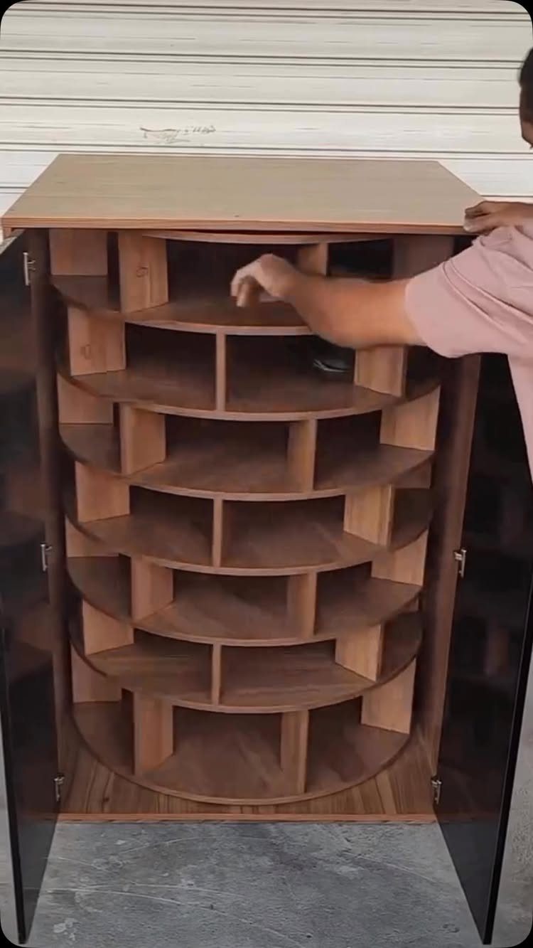 A person reaching into a large, curved wooden shelving unit with multiple semicircular compartments.