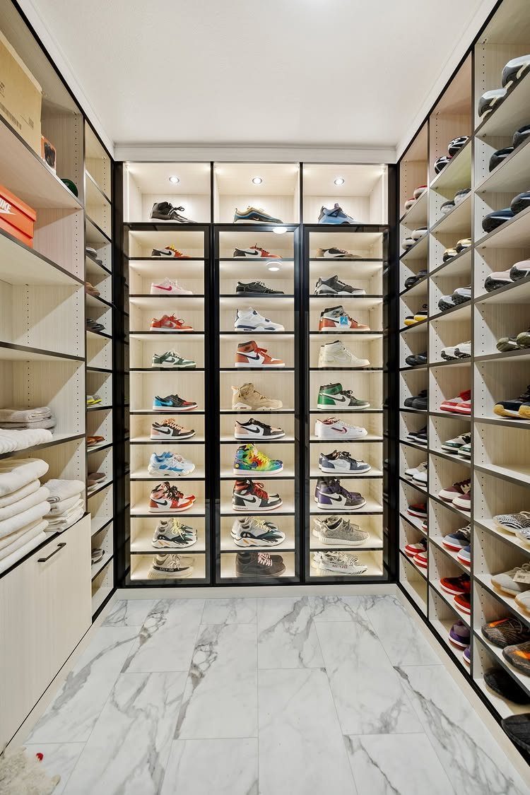 Built-in white closet shelving units filled with many pairs of colorful sneakers in a marble floor room.