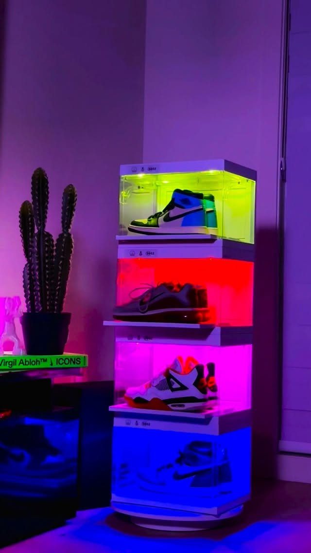 A glowing neon multi-colored shoe storage rack displaying several pairs of sneakers in a dark room.