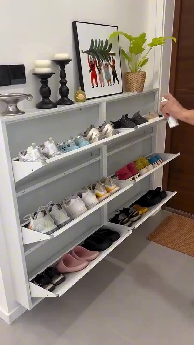 White multi-tiered shoe storage cabinet with slanted shelves holding various pairs of sneakers.