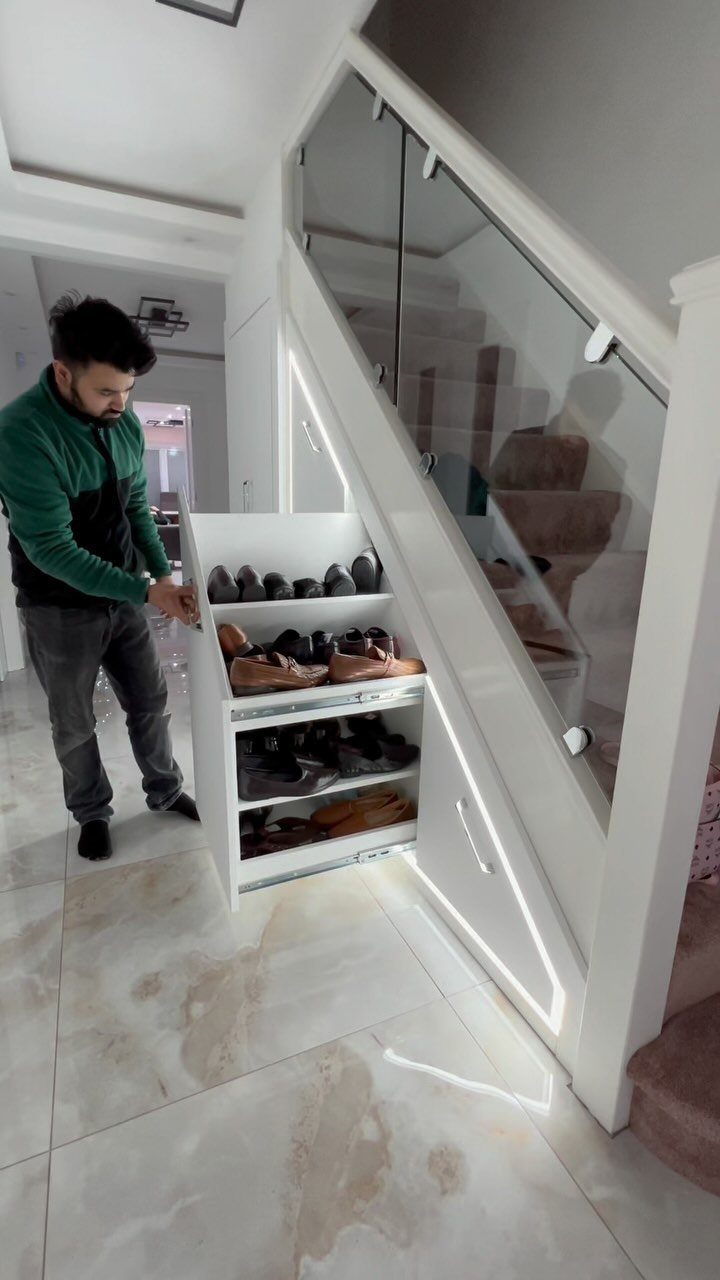 A man stands beside a white built-in shoe storage unit under a staircase filled with shoes.