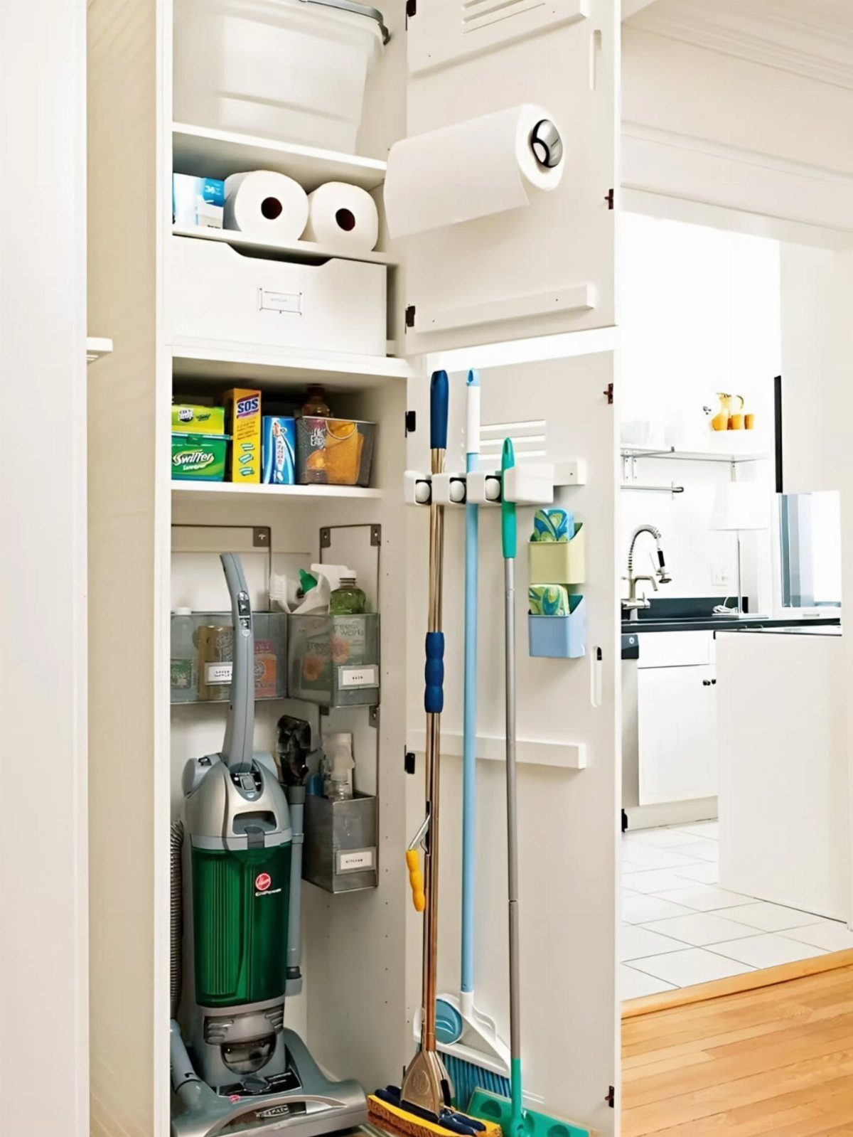A white pantry closet filled with cleaning supplies, a vacuum, and tools hanging on the door.