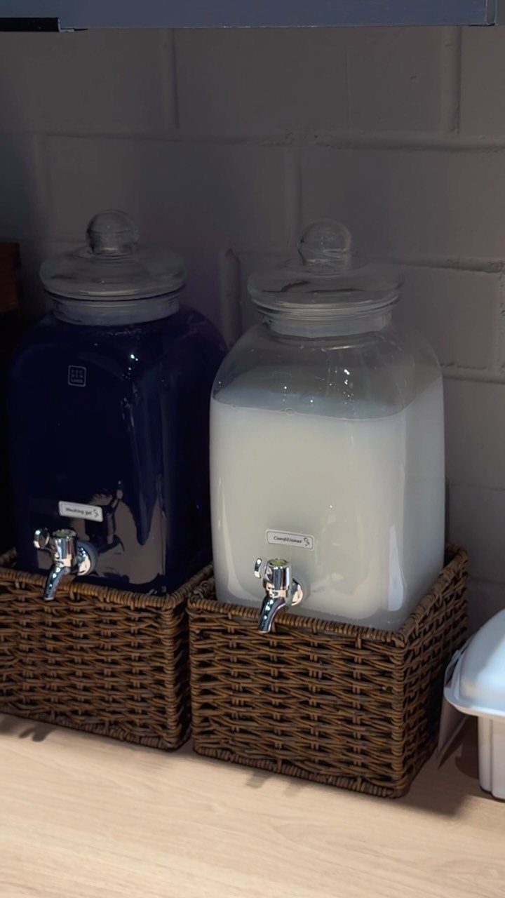 Two large glass beverage dispensers with spigots sitting in brown wicker baskets.
