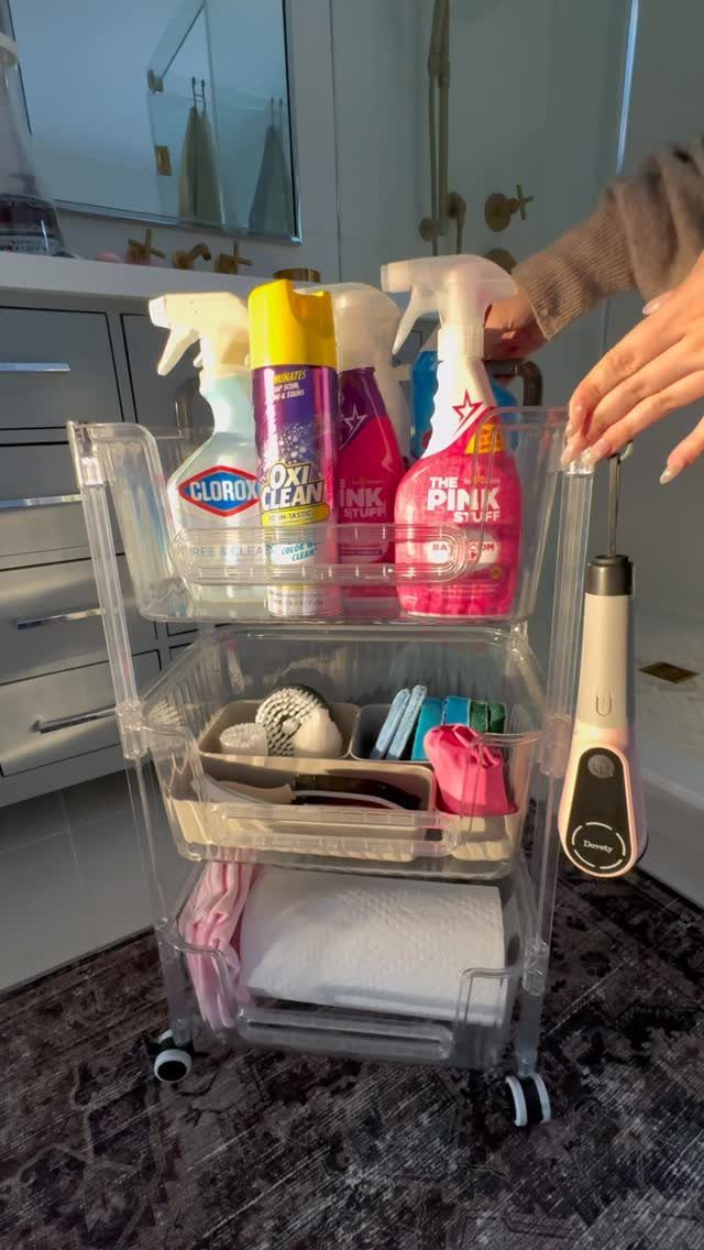 A clear plastic rolling cart filled with various colorful cleaning spray bottles and supplies.