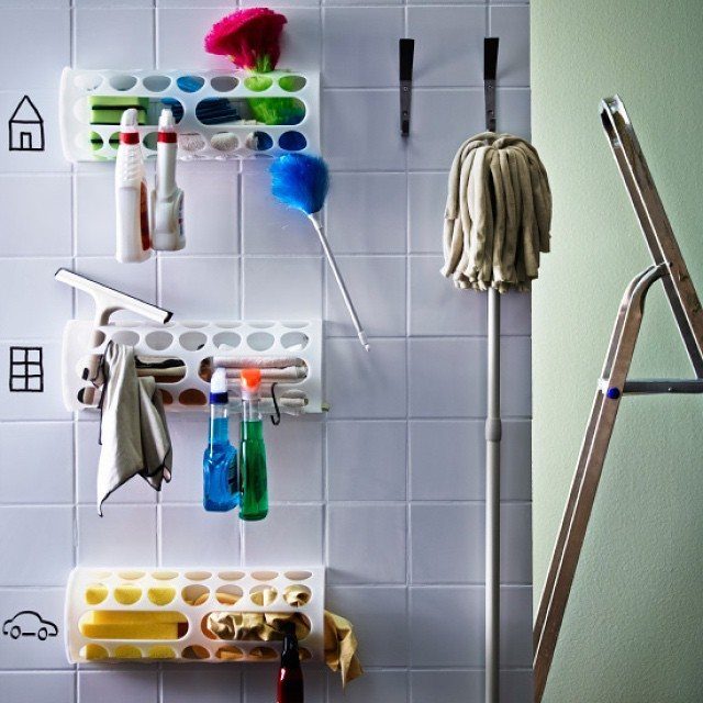 Cleaning supplies organized in white wall-mounted holders on a white tiled wall next to a mop.