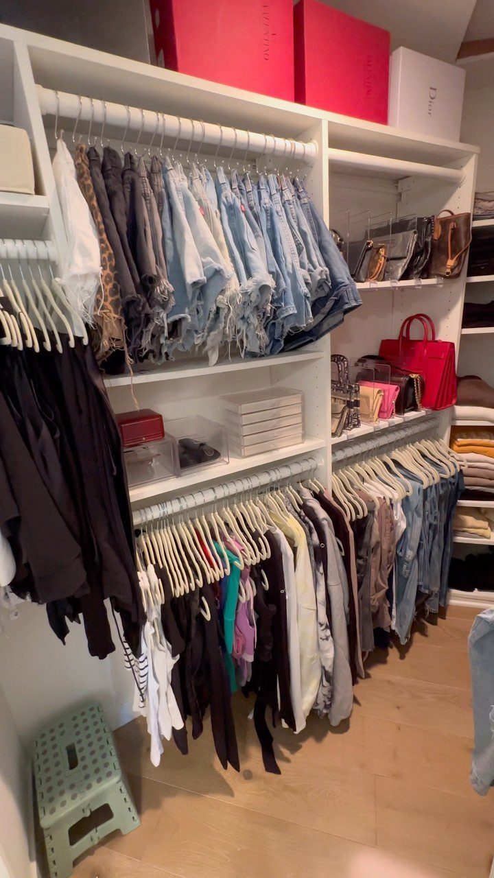 White built-in closet with hanging clothes, denim shorts, and various accessories on shelves.