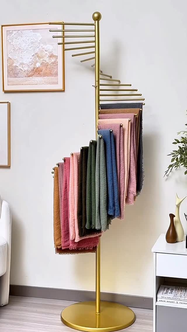 Gold metal scarf rack holding various colorful folded fabrics against a white wall.