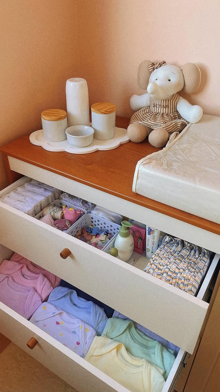 Open white dresser drawers containing organized baby clothes and small items in white plastic bins.