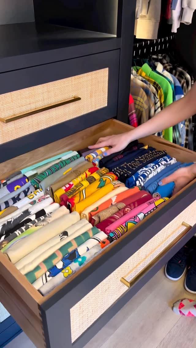 Hands organizing colorful clothes folded vertically in an open wooden dresser drawer.