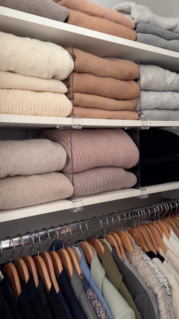 Folded neutral-colored knitwear sweaters organized on white shelves with clear acrylic dividers.