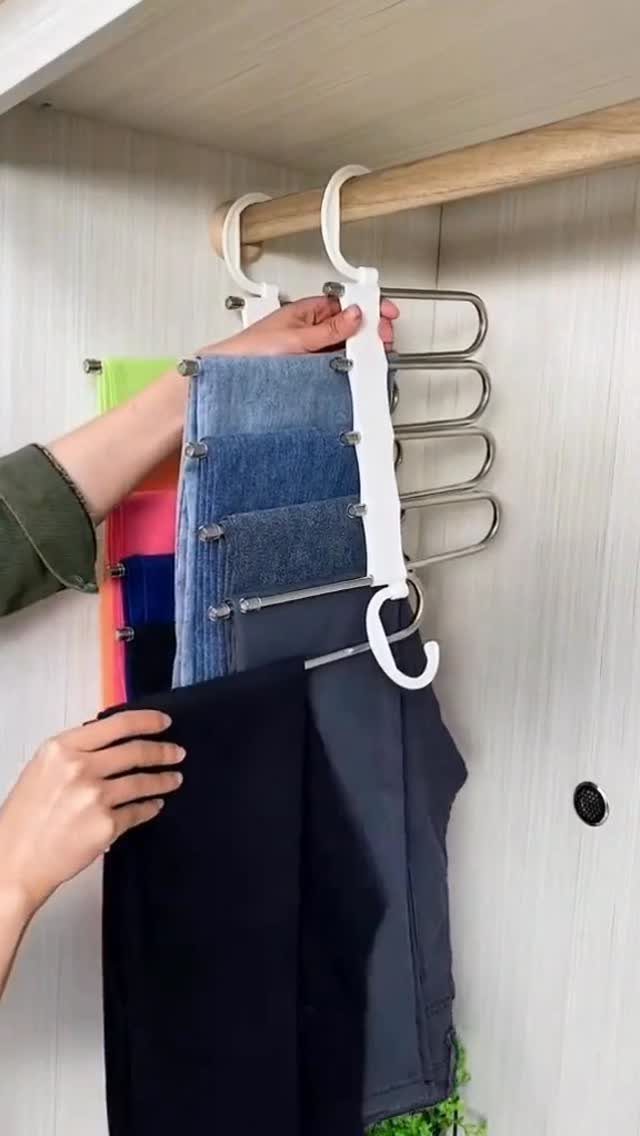 Hands hanging a multi-tiered white hanger with folded denim jeans onto a wooden closet rod.