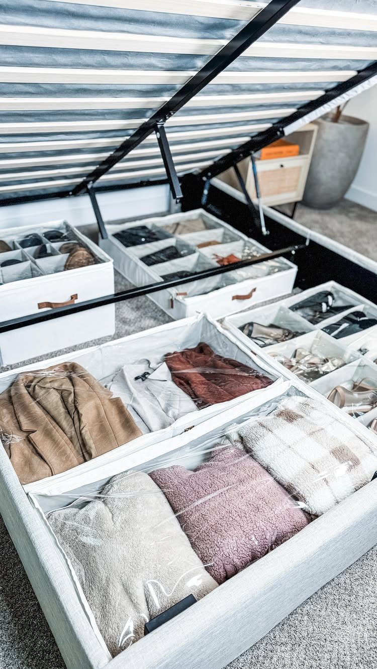 White fabric storage bins filled with folded clothes organized under a bed frame.