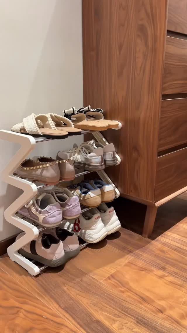 White zig-zag vertical shoe rack holding various pairs of footwear on a wooden floor.