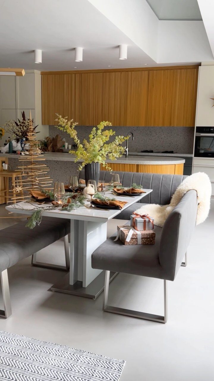A modern dining set with a marble table, grey chairs, and a long grey upholstered bench.