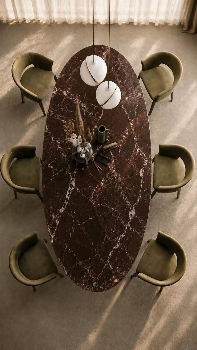 An oval dark marble dining table surrounded by six olive green chairs in a sunlit room.