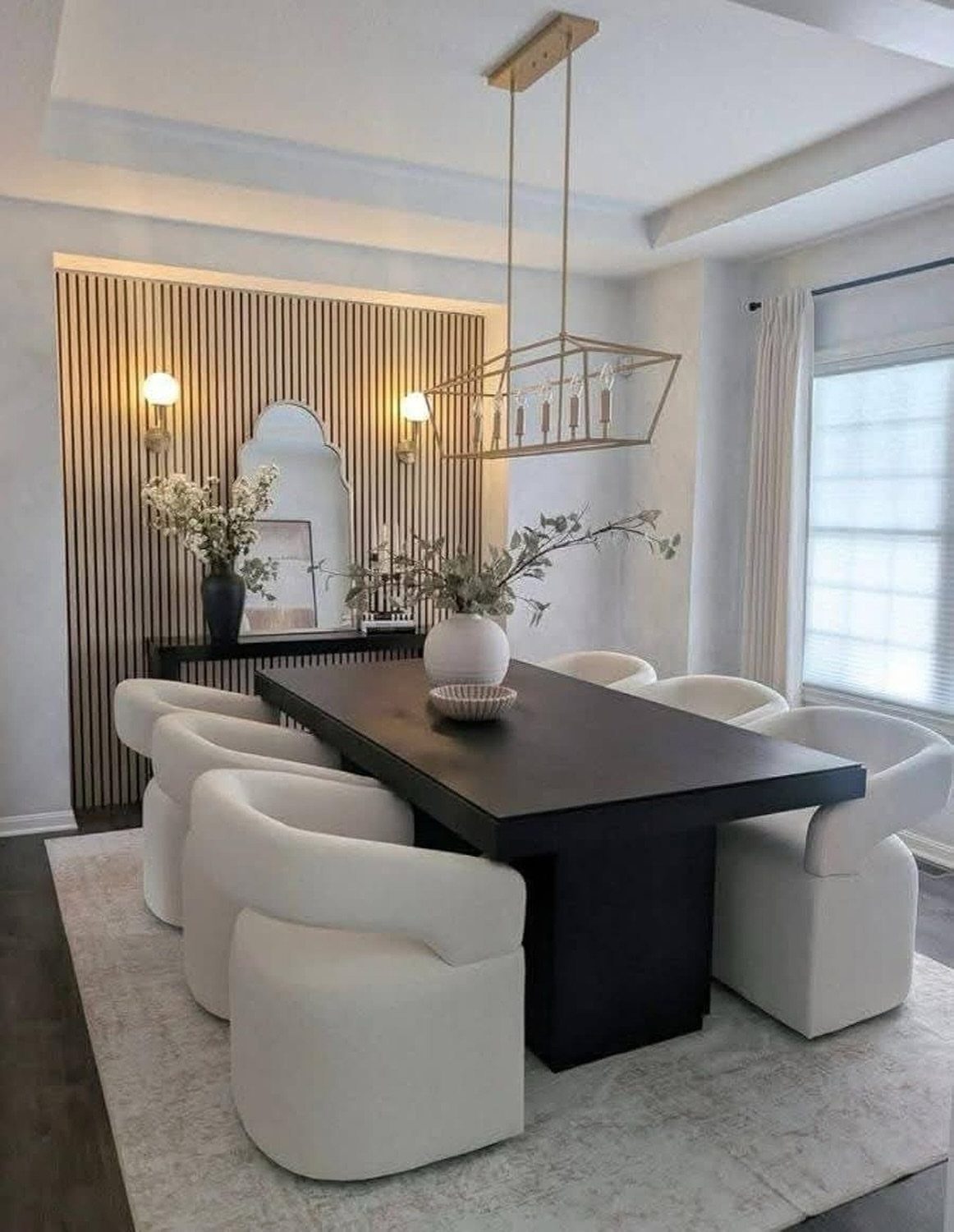 A dark dining table with white chairs sits on a light rug in a neutral room.