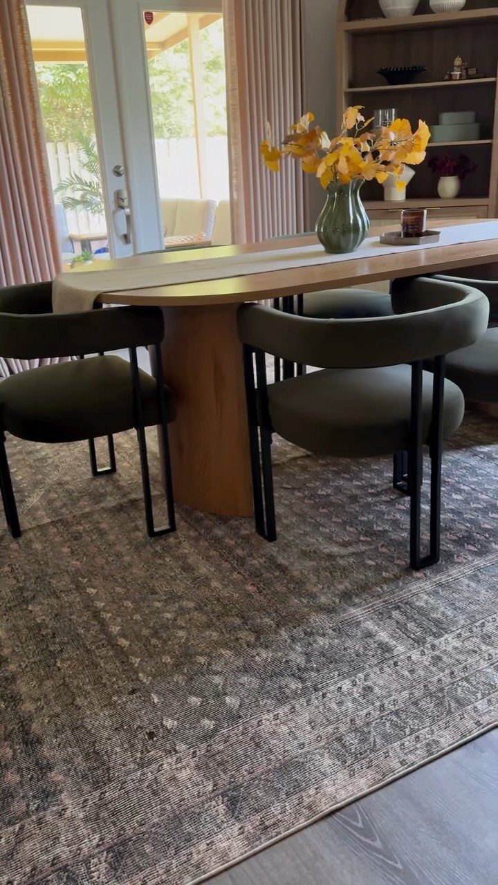 A patterned grey rug underneath a wooden dining table and dark green chairs.