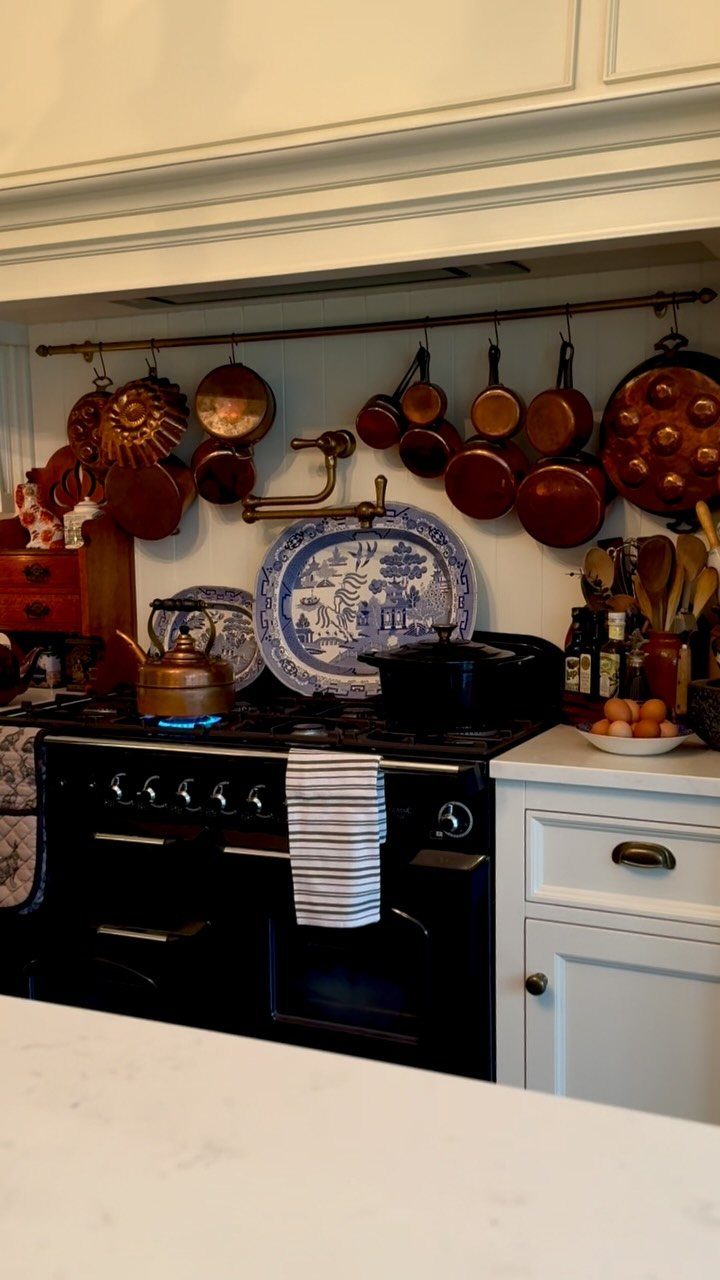 White Shaker cabinets and a black stove with hanging copper pots in a kitchen.