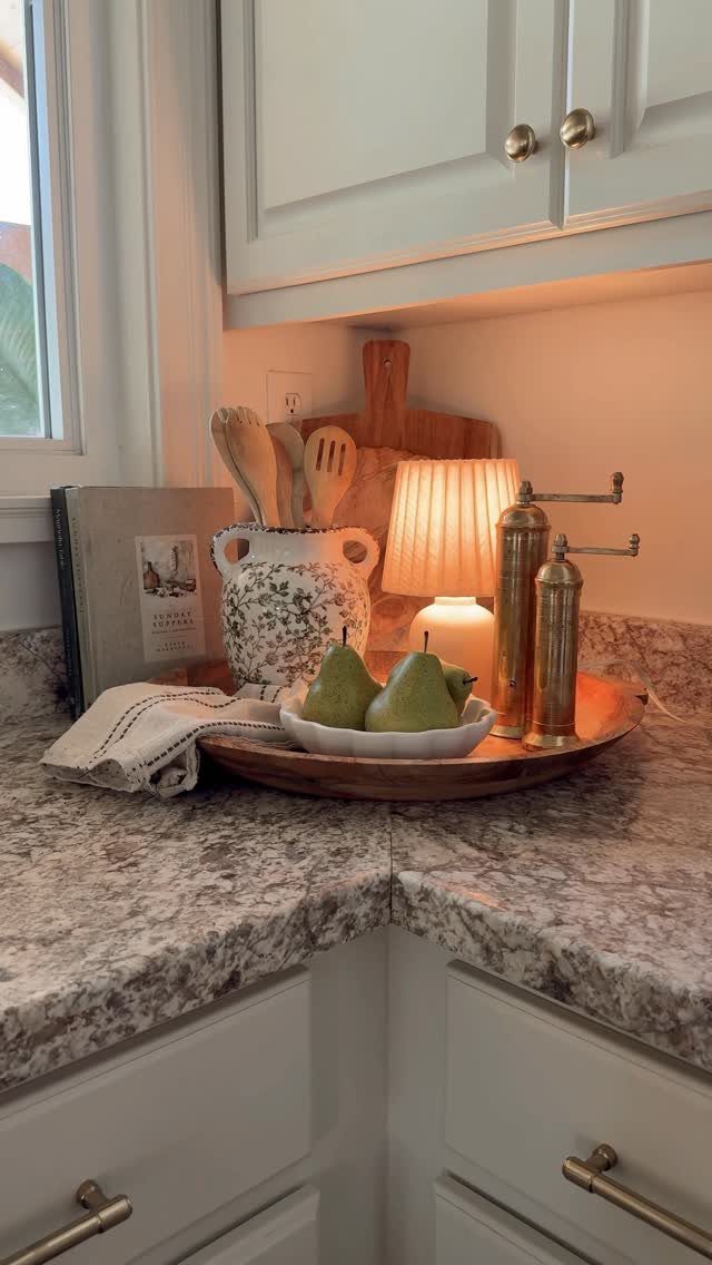 Kitchen countertop decor featuring pears, wooden utensils, and a small lamp in warm tones.