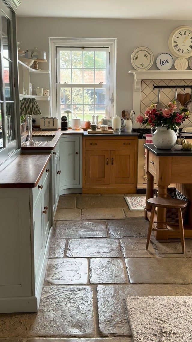 A rustic farmhouse kitchen with blue cabinets, wooden counters, and large stone floor tiles.