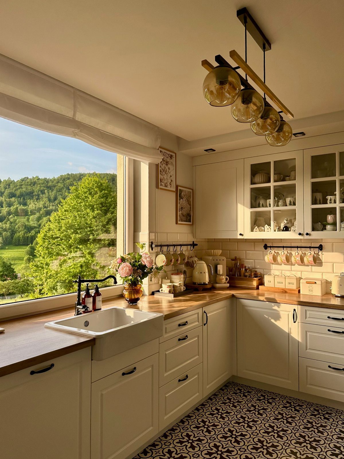 A bright farmhouse kitchen with white cabinets, wooden counters, and a view of green hills.