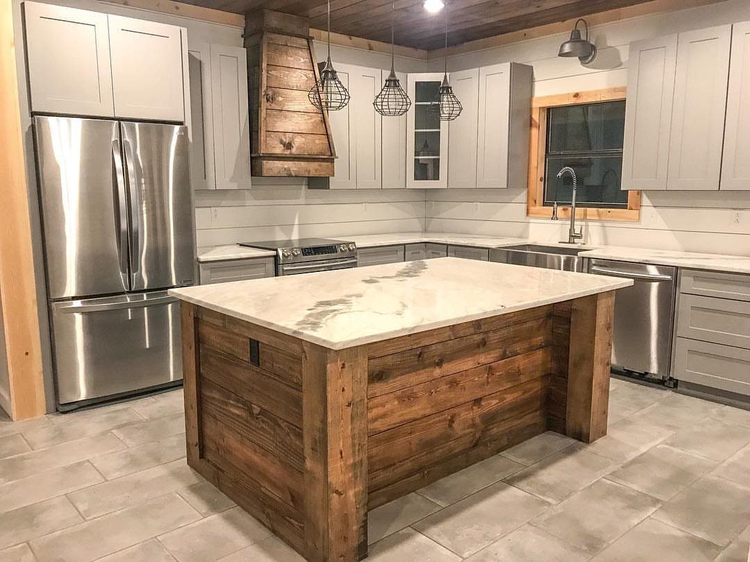 A farmhouse kitchen with a wooden island, grey cabinets, and white shiplap walls.