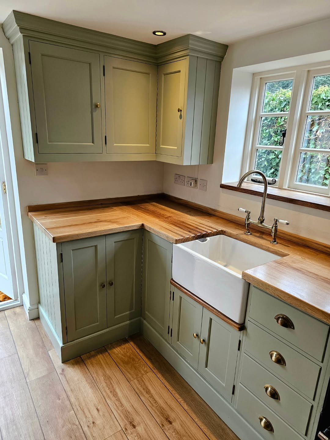 Sage green kitchen cabinets with butcher block countertops and a white farmhouse sink.
