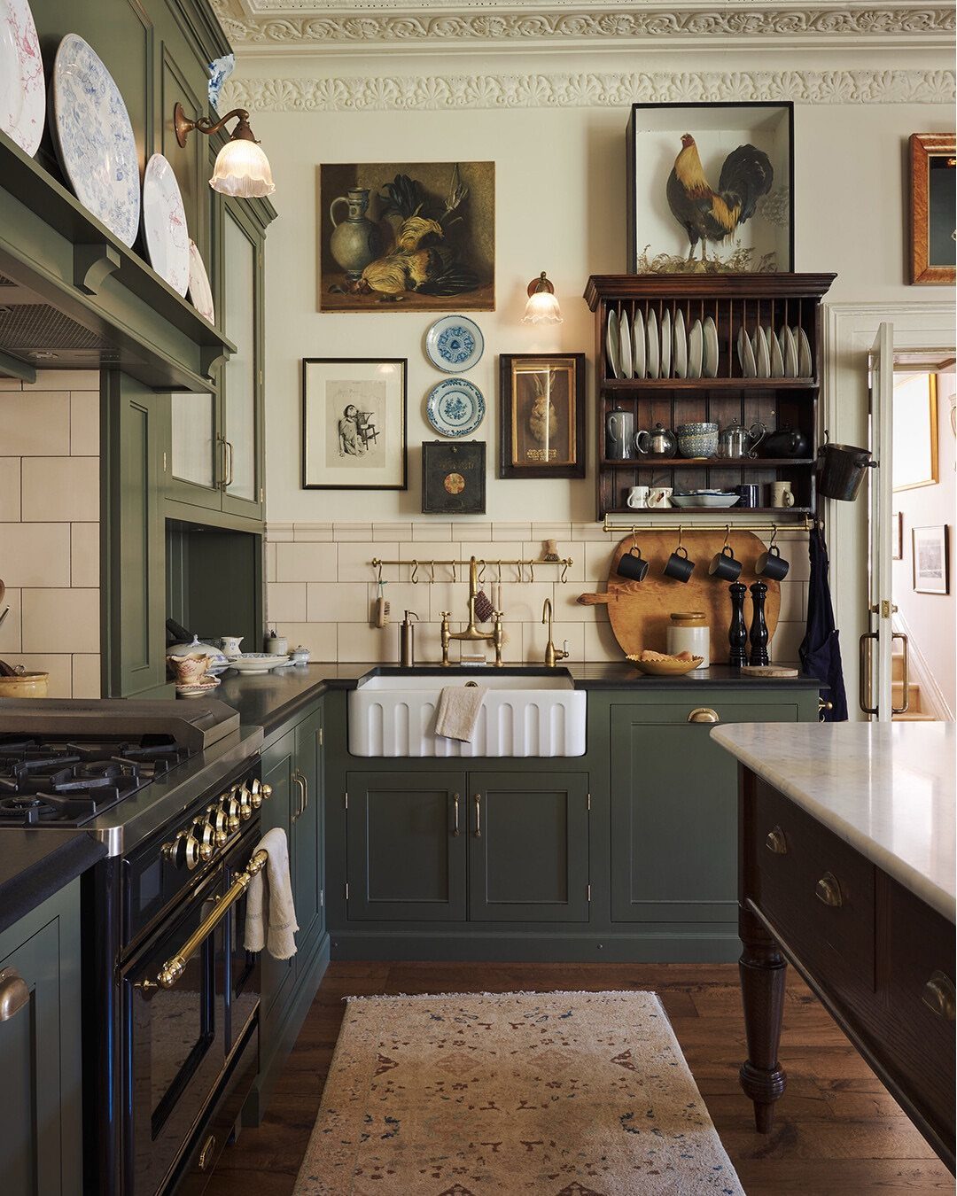 Sage green kitchen cabinets surrounding a white apron-front sink and a dark stove.