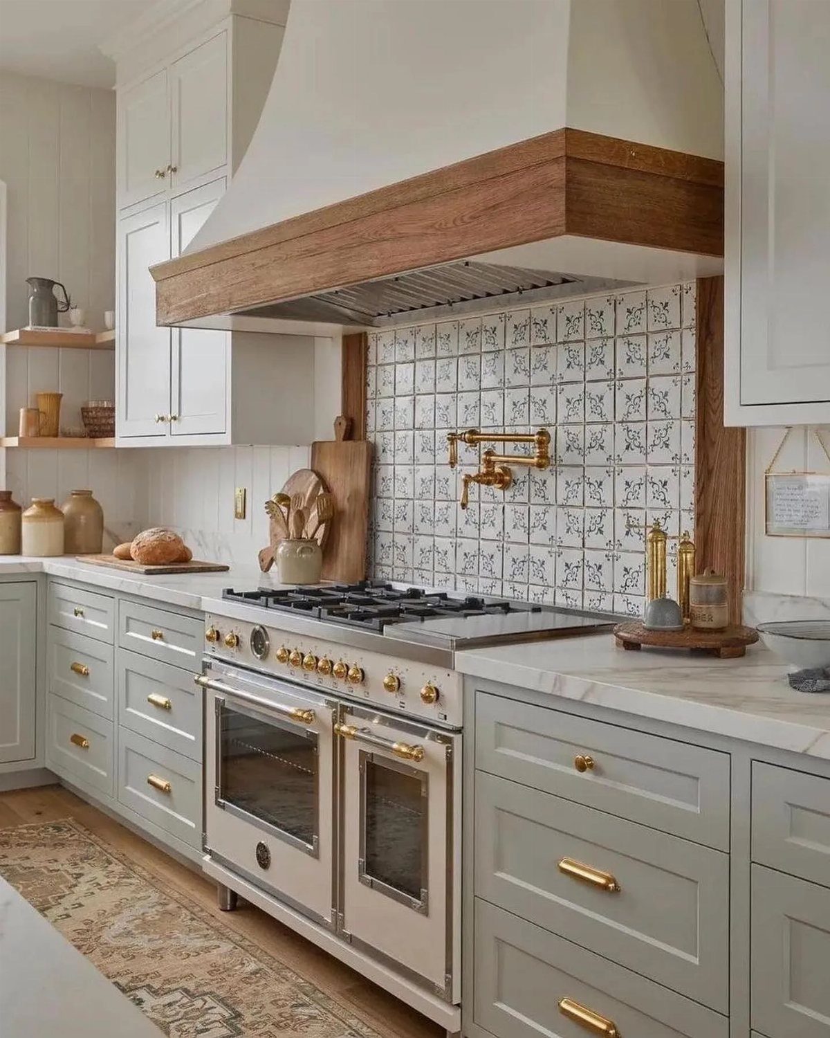 Sage green kitchen cabinets with brass hardware, marble countertops, and a patterned tile backsplash.