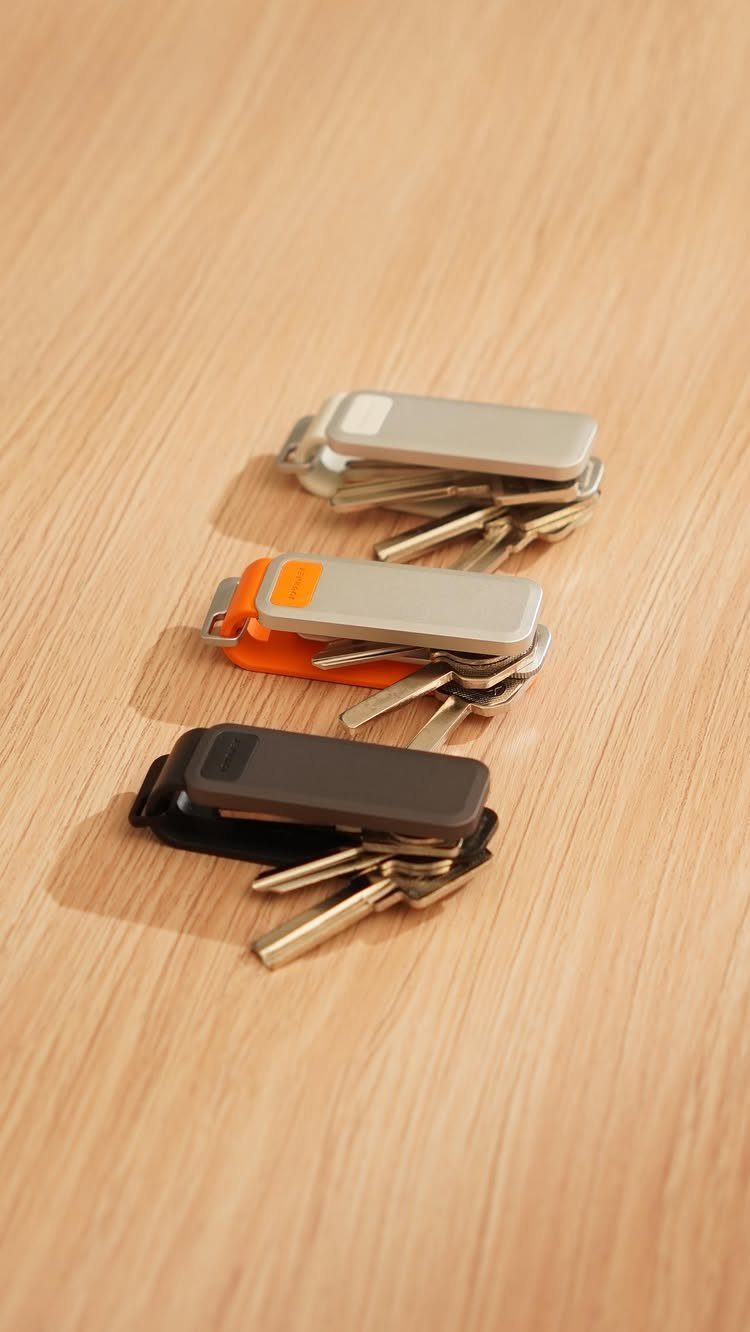 Three sets of organized metal keys with different colored rectangular holders on a wooden table.