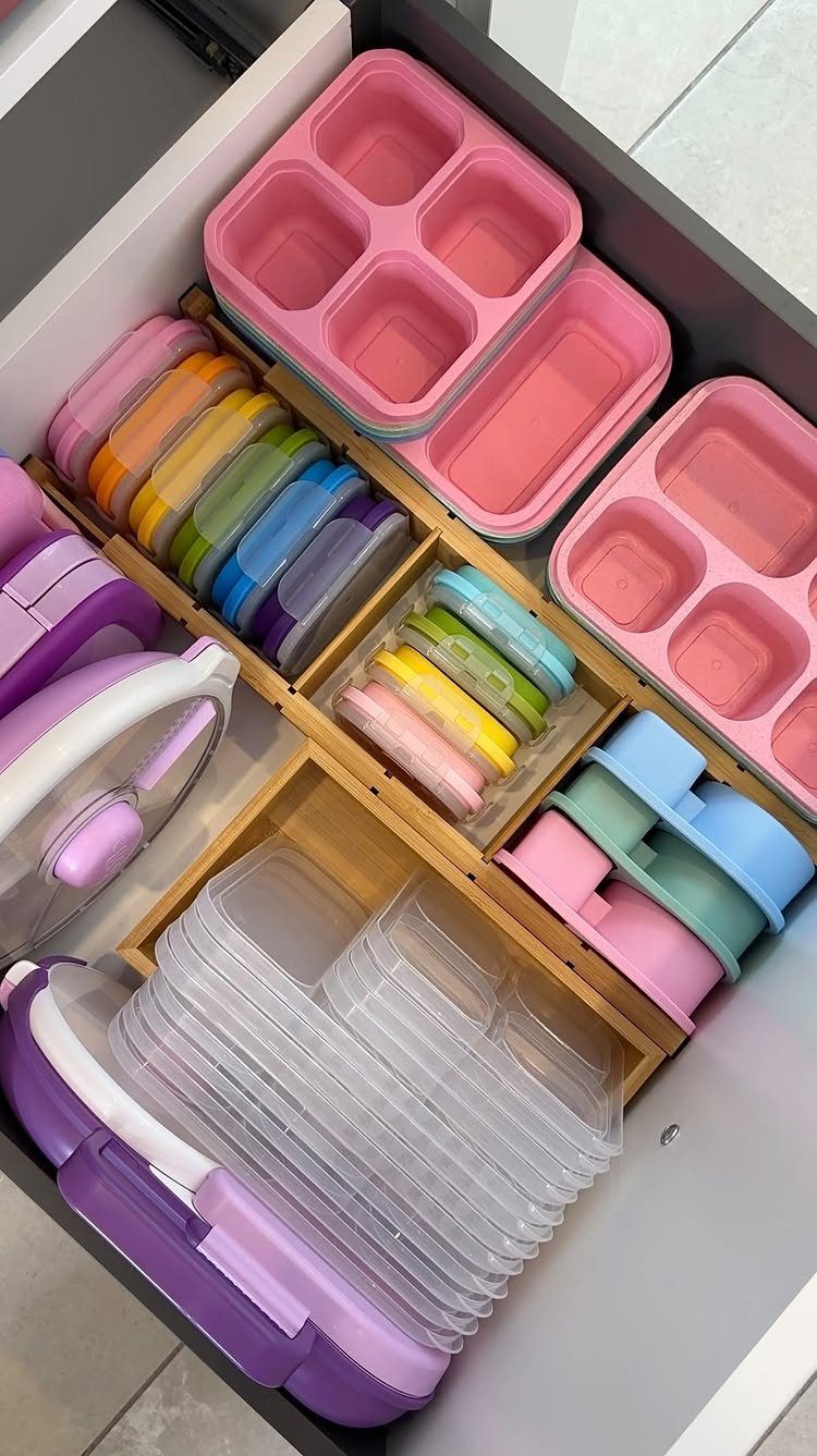 Organized kitchen drawer containing various colorful plastic food storage containers in wooden dividers.