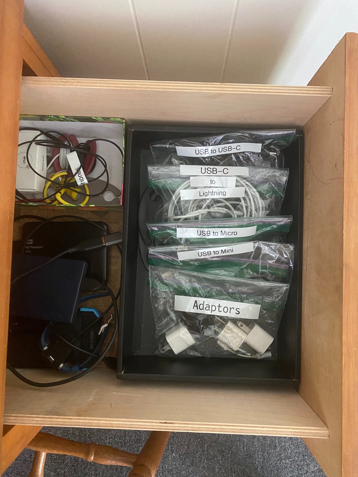 Organized electronic cables and adapters stored in labeled plastic bags inside a black tray.