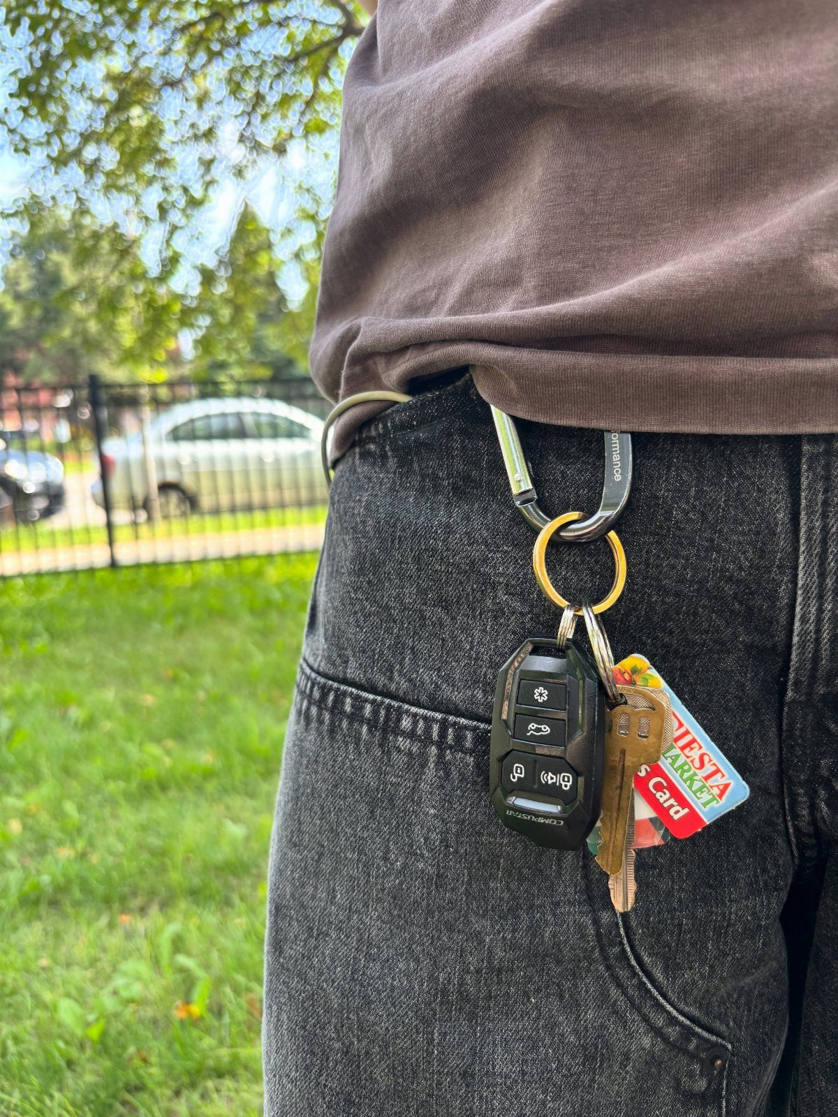 A silver carabiner clipped to a belt loop holding several keys and a red card.