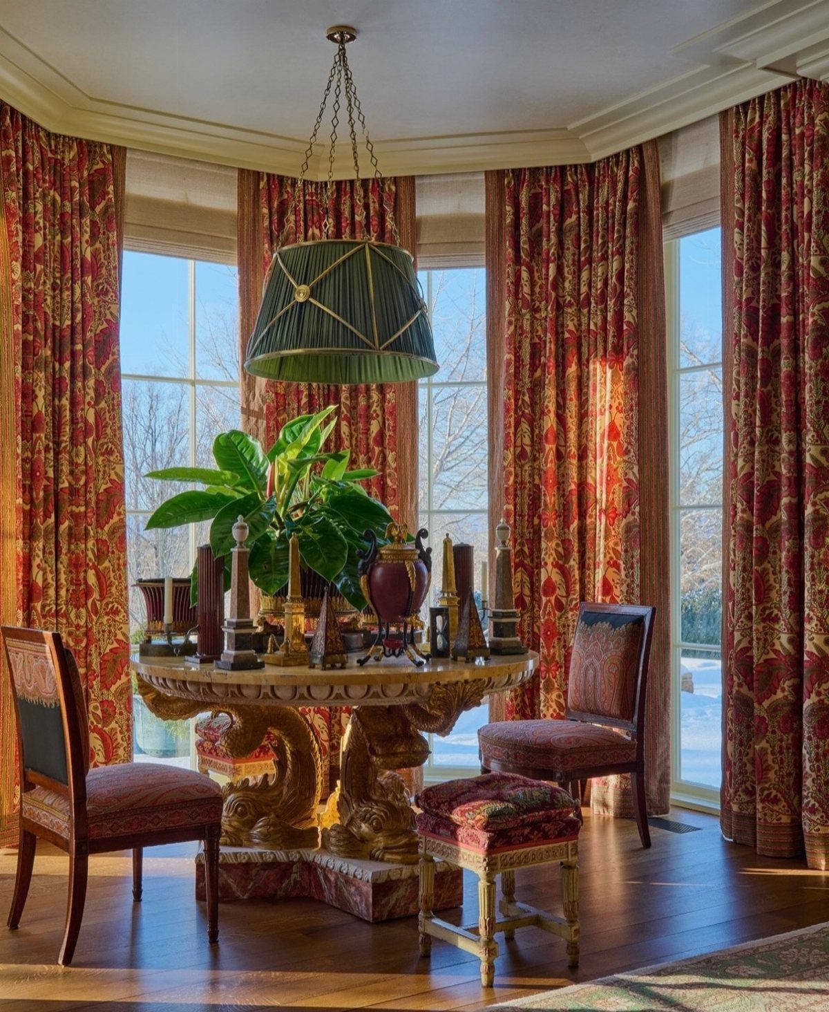 Ornate marble dining table with gold legs surrounded by patterned chairs and red curtains.