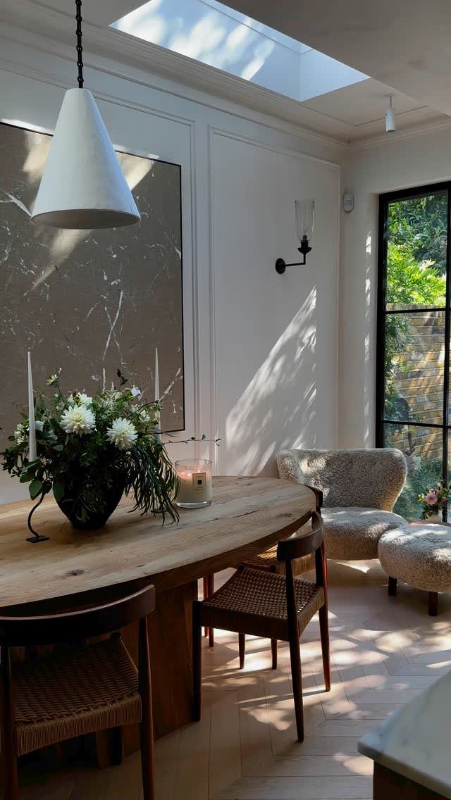 A wooden dining table with a lush green and white floral centerpiece in a sunlit room.