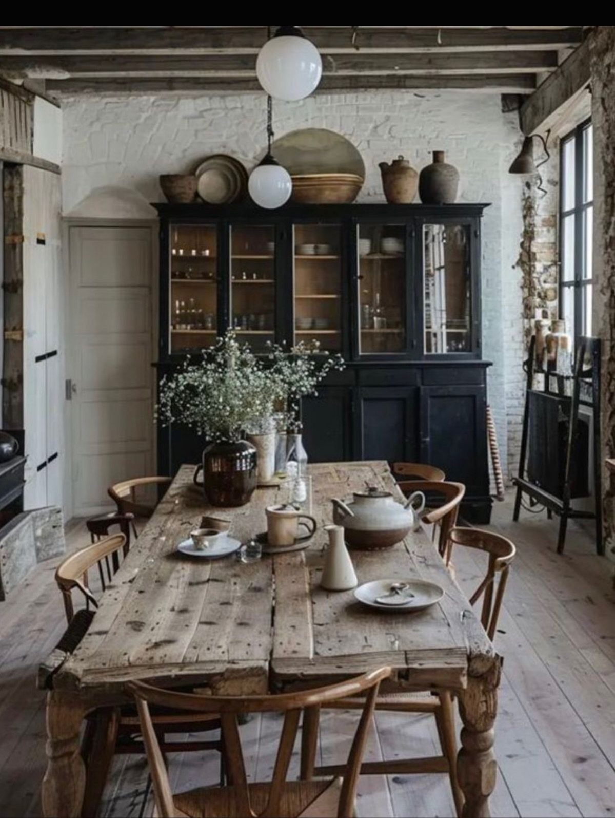 A rustic dining room with a long wooden table, black hutch, and eclectic ceramic decor.