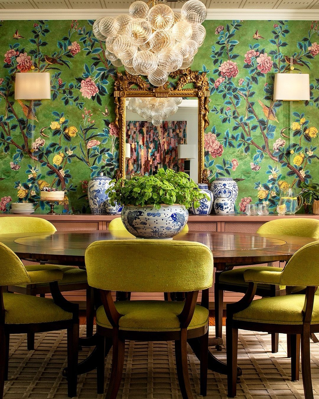 Eclectic dining room with green floral wallpaper, gold mirror, and lime green chairs around a wooden table.