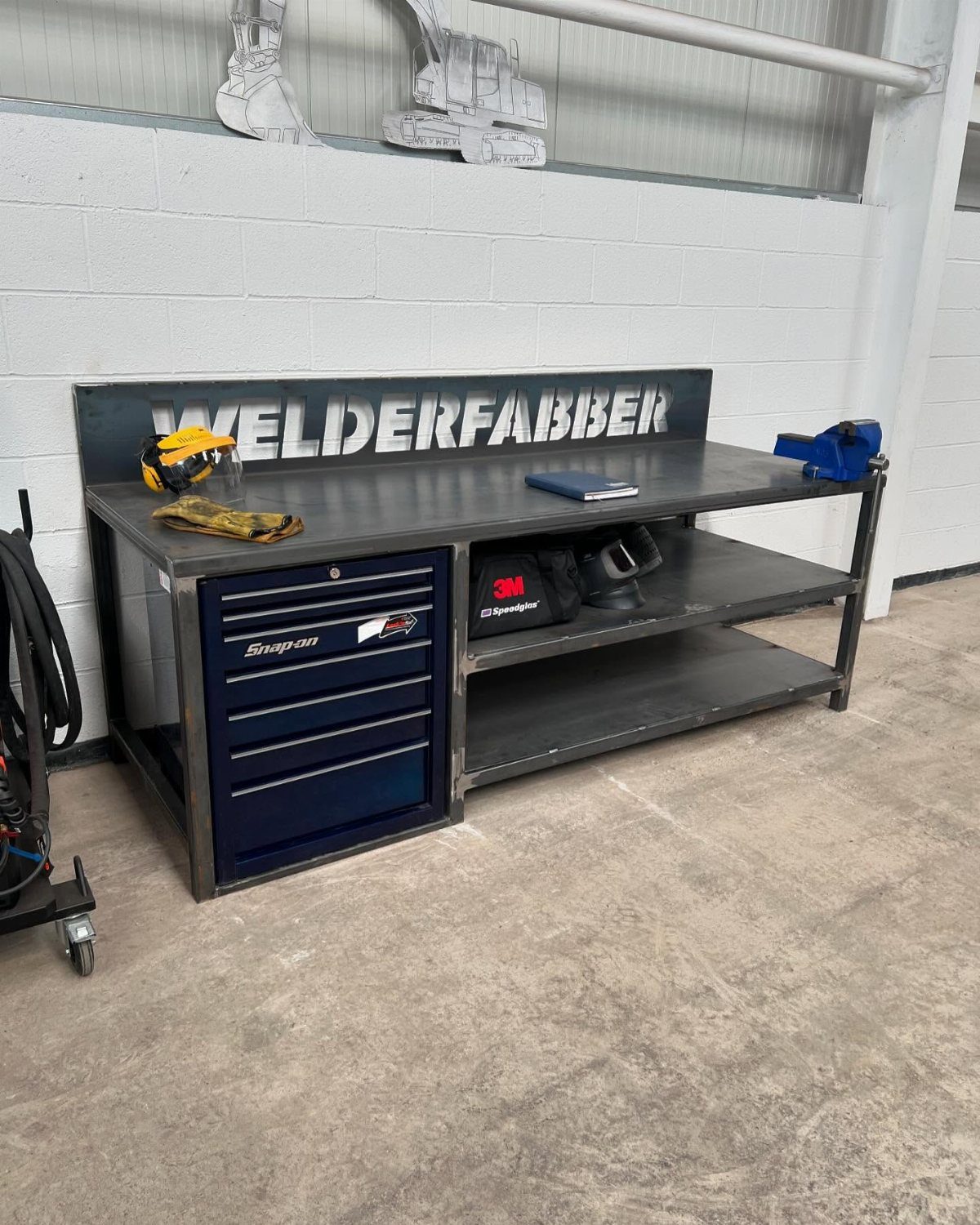 A heavy-duty metal workbench with a steel frame and integrated blue tool chest in a garage.