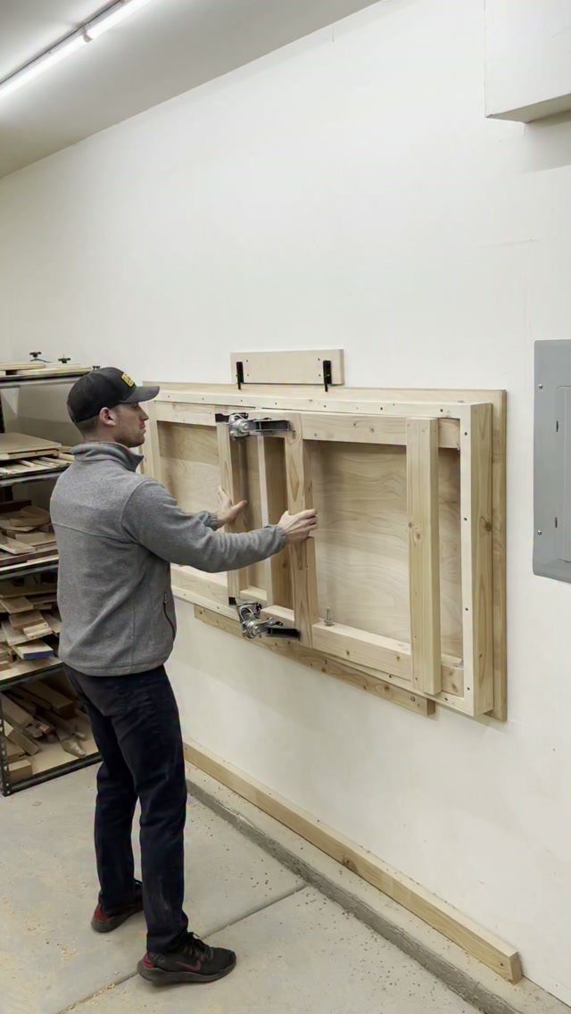 A man unfolding a wooden folding workbench mounted to a white garage wall.