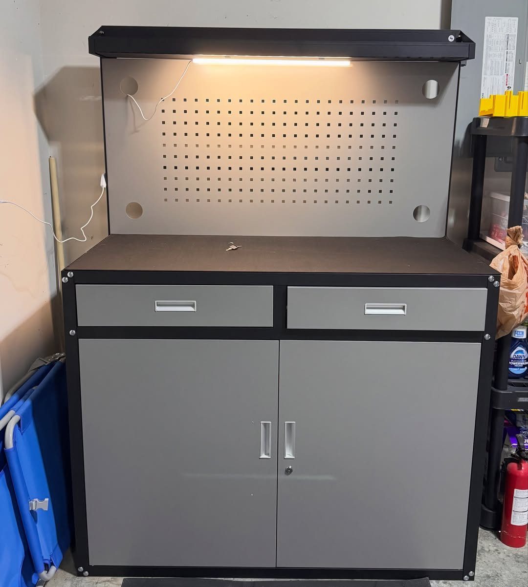 A grey garage workbench featuring a pegboard, integrated lighting, and storage cabinets.