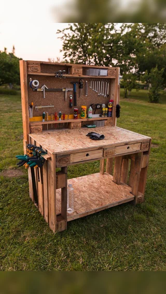 A handmade wooden workbench constructed from pallets with tools organized on a pegboard backboard.