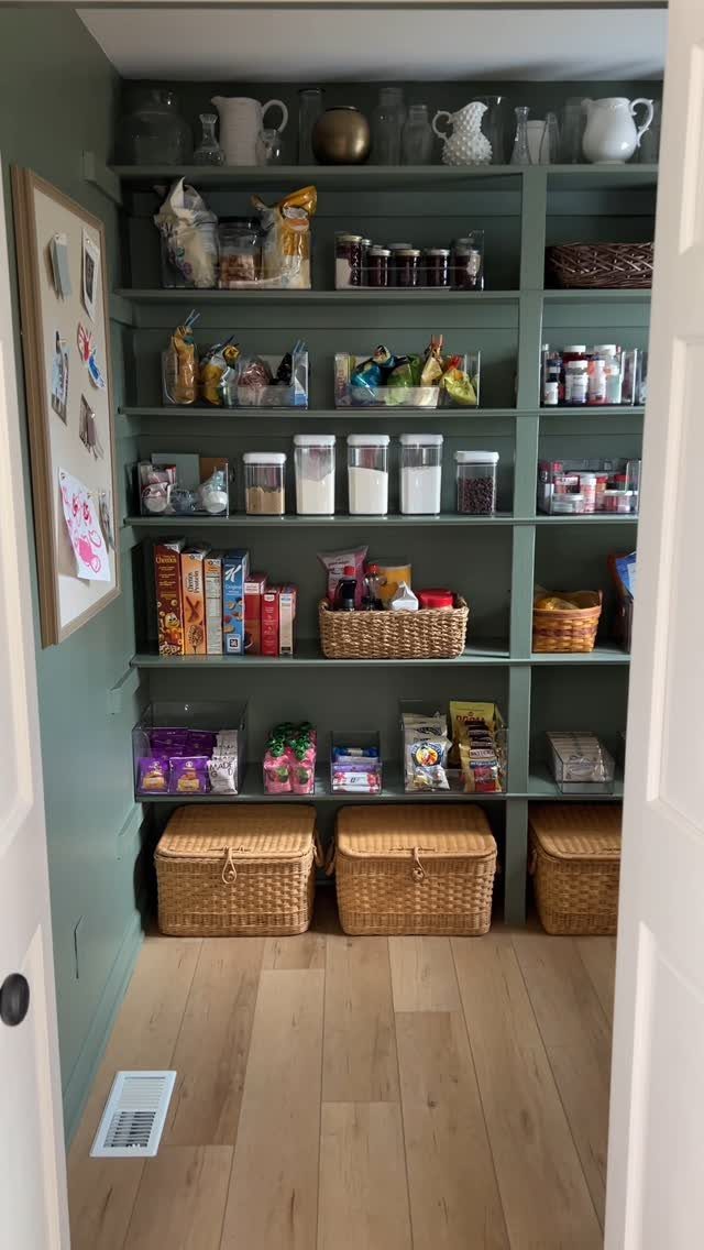 Sage green built-in pantry shelves stocked with organized food containers and wicker baskets.