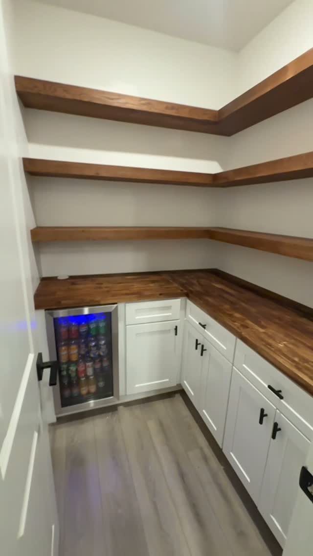 A pantry with white cabinets, a beverage fridge, and butcher block countertops and shelves.