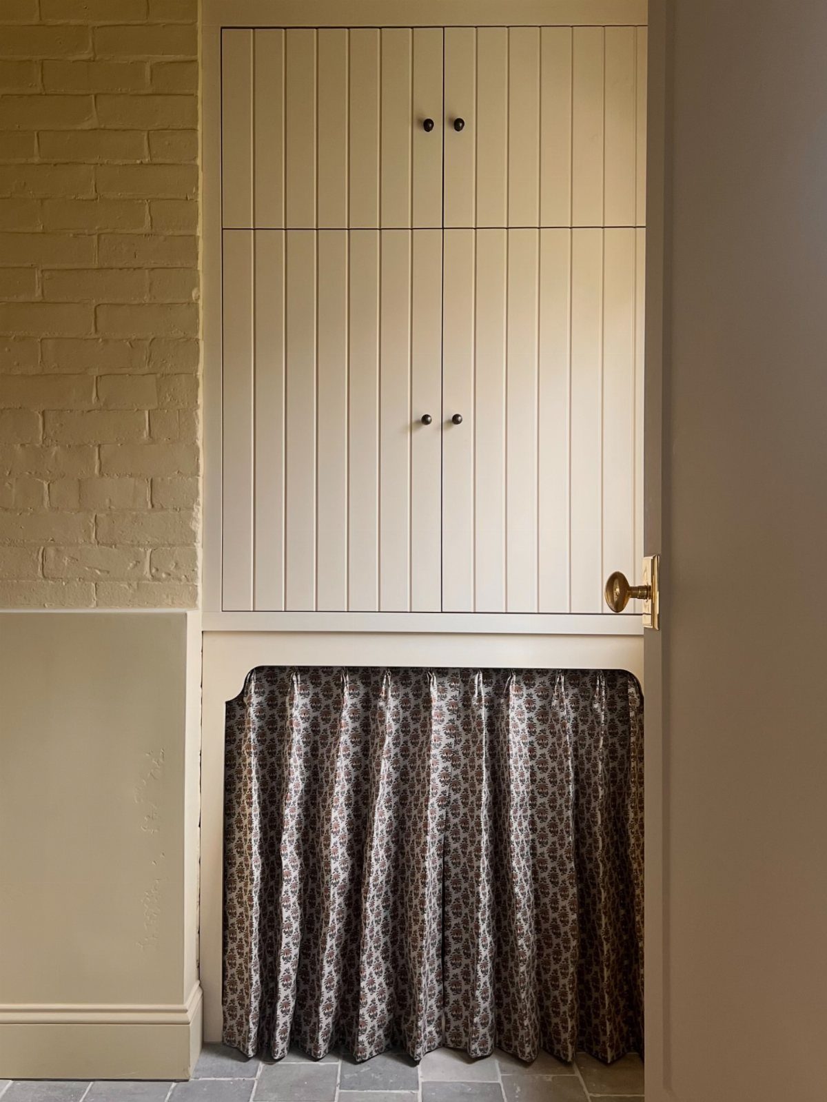 Cream paneled pantry cabinets with a leopard print cafe curtain covering the lower half.