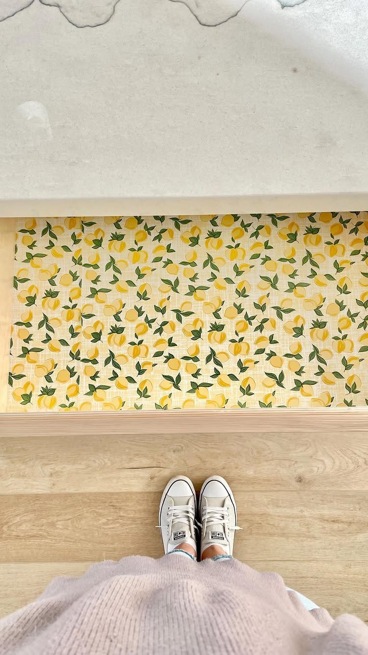 A drawer lined with bright yellow lemon pattern contact paper next to a person's feet.