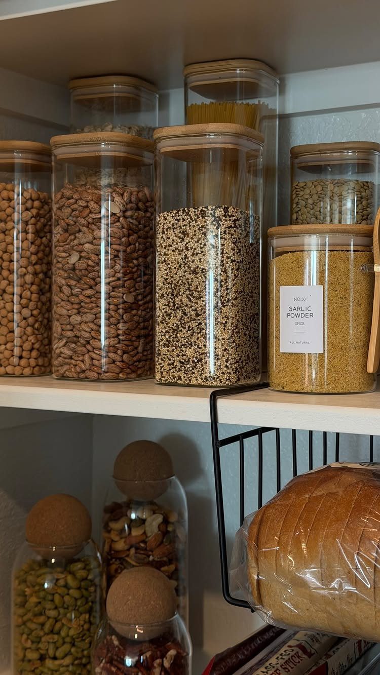 Glass jars filled with grains and nuts organized on white pantry shelves.