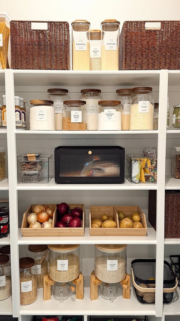 White pantry shelves organized with glass jars, wooden produce crates, and woven wicker baskets.