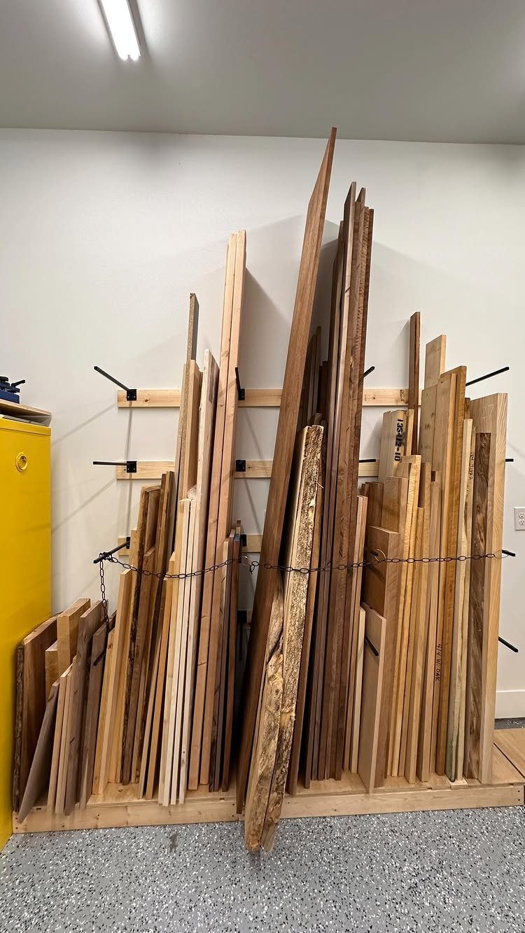 Various wooden planks stored vertically in a wooden rack against a white garage wall.