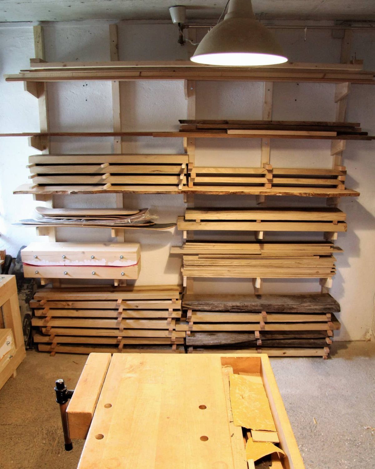 Wooden wall-mounted shelving unit filled with various planks and lumber in a workshop setting.